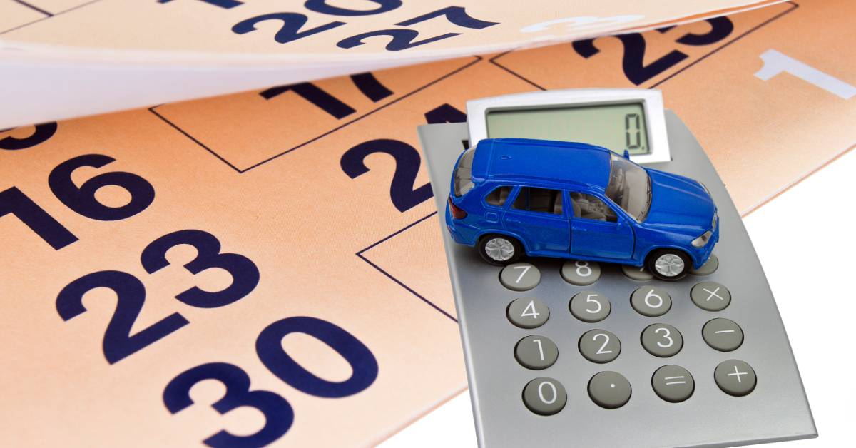 A close-up of a blue, toy car resting on a calculator on top of a calendar with a page flipped over it.