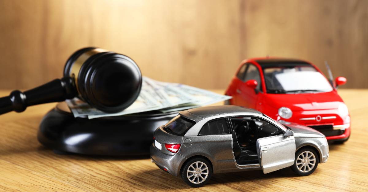 Two toy cars, one red and one silver, collide on top of a desk next to a gavel resting on a pile of money.