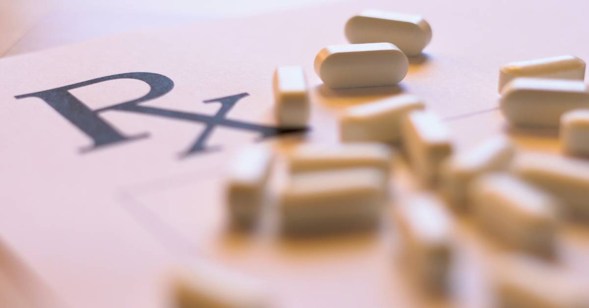 A close-up of a prescription form with the letters "RX" and several white tablet pills scattered across the surface.