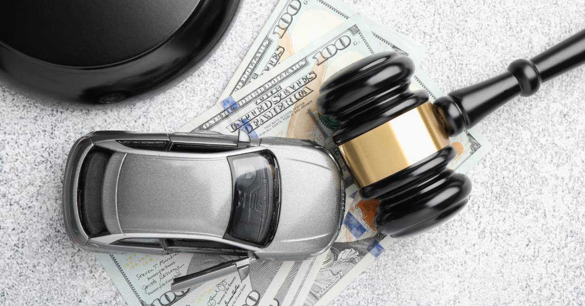 A close-up of a gavel and silver model car resting on top of a pile of one-hundred-dollar bills on a desk.