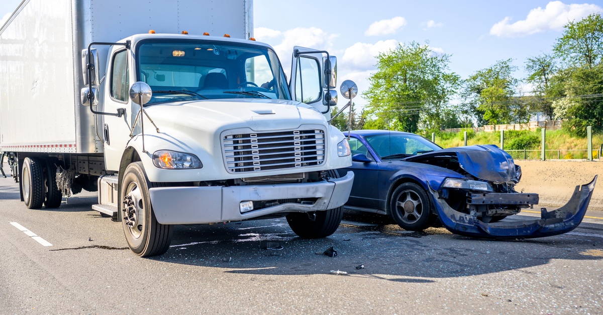 A semu truck and a blue passenger car parked next to each other after an accident. The blue car has taken significant damage.