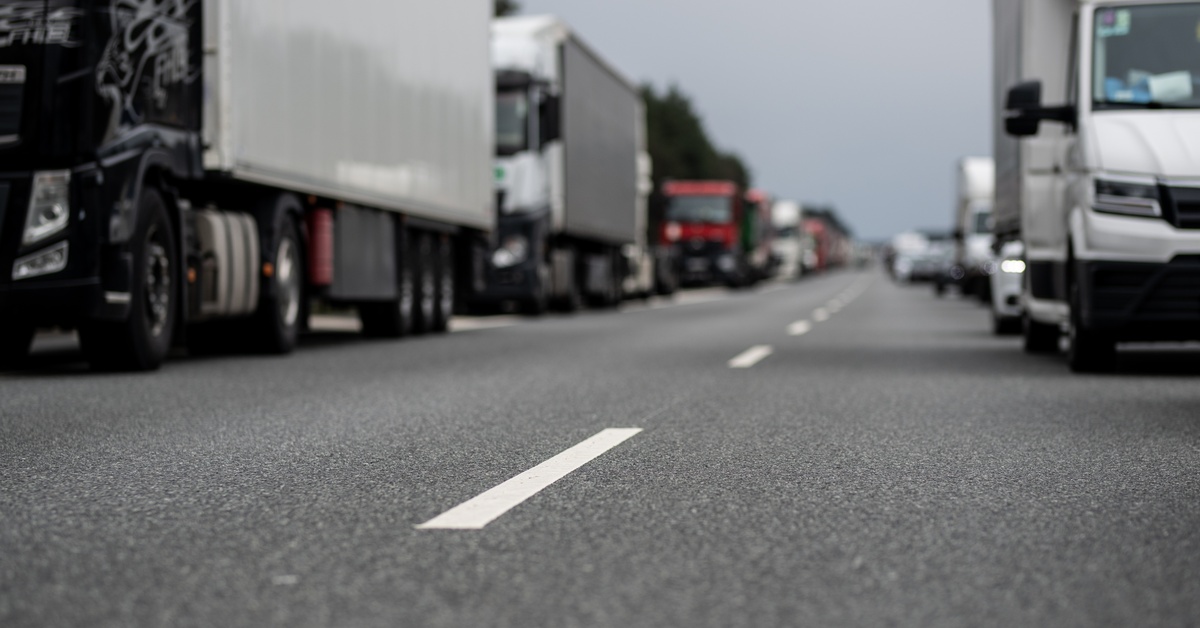 A close-up of the middle white lines on a paved road with rows of semi trucks driving down the lanes on either side.