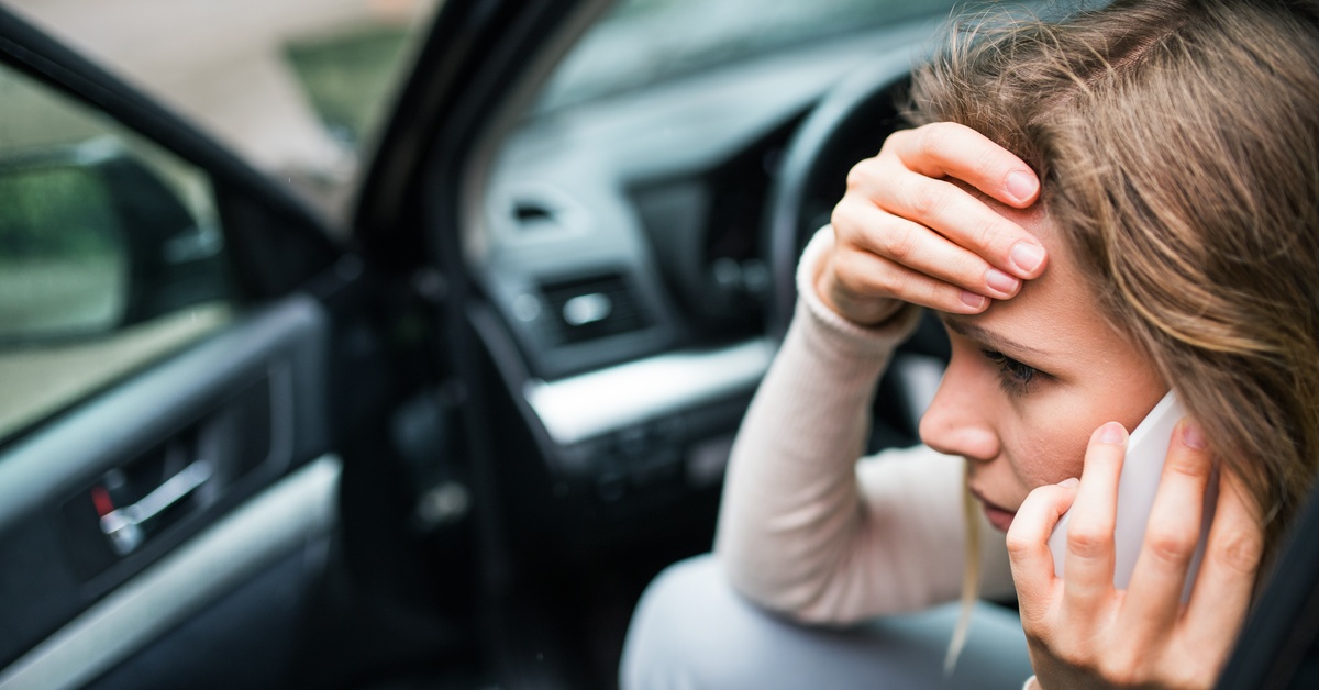 A close-up shows a woman sitting half-in, half-out of a vehicle while on the phone. She has a hand on her forehead.