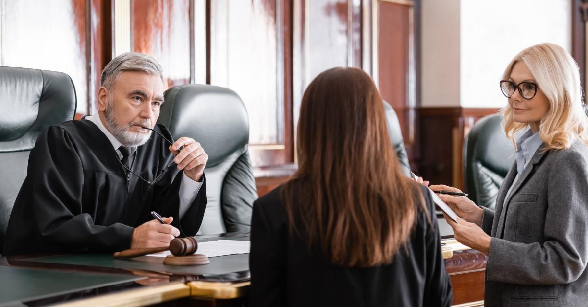 A lawyer standing with a client in front of a judge's podium in a courtroom, all of them dressed very professionally.